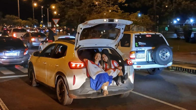 Mujeres sonrientes con camisetas de la selección paraguaya, sentadas en el maletero de un automóvil blanco en la Costanera.