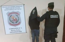 Hombre con capucha negra siendo escoltado por un oficial en uniforme policial en comisaría de Encarnación.