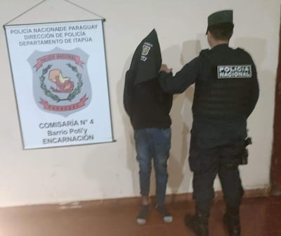 Hombre con capucha negra siendo escoltado por un oficial en uniforme policial en comisaría de Encarnación.