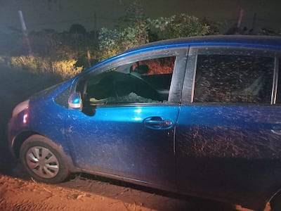Automóvil azul sucio y desgastado con ventana rota, estacionado en un entorno rural y rodeado de vegetación.