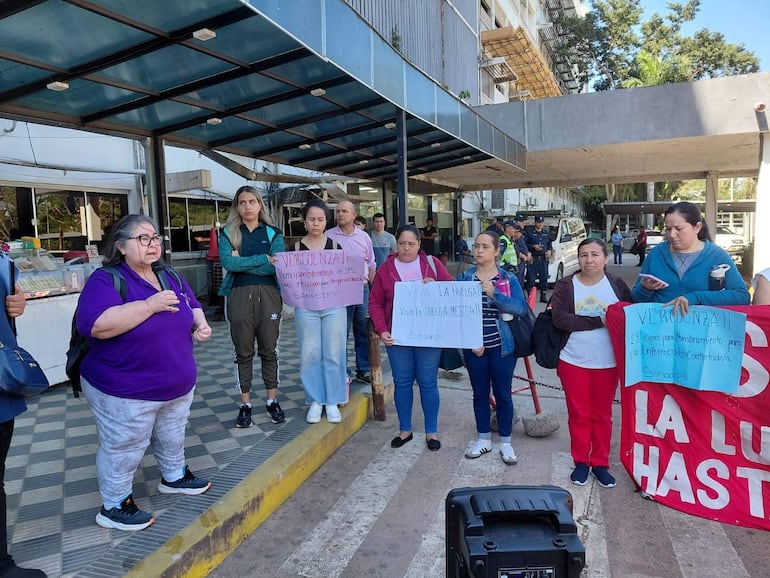 Mujeres de Sinadips sosteniendo carteles y gesticulando en protesta, lucen ropa casual, frente al Hospital Central del IPS.