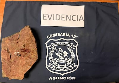 Roca manchada de sangre sobre una tela con el escudo de la Policía Nacional en un ambiente interior.