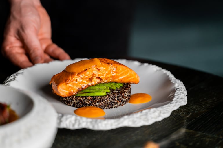 Filete de salmón sellado servido sobre una base de quinoa negra y rodajas de aguacate.