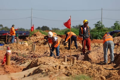 Seis trabajadores en un sitio de construcción, con cascos amarillos y chalecos naranjas, excavando en terreno de tierra.