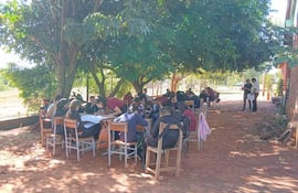 Grupo de jóvenes sentados al aire libre bajo un árbol, algunos escribiendo, otros discutiendo, con ambiente informal de estudio.
