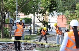 Cinco trabajadores en construcción, usando cascos y chalecos naranjas, rodeados de árboles y escombros.