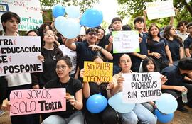 Grupo de jóvenes con carteles de protesta, entre ellos una mujer con gafas y un cartel rosa. Ambiente de manifestación educativa.