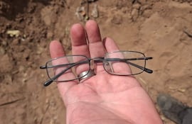 Mano mostrando anteojos de metal con cristales transparentes sobre suelo seco y arenoso.