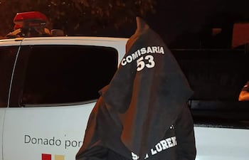 Persona arrestada con bolsa en la cabeza, sudadera negra 'COMISARIA 53', esposado frente a una camioneta de Itaipú Binacional.
