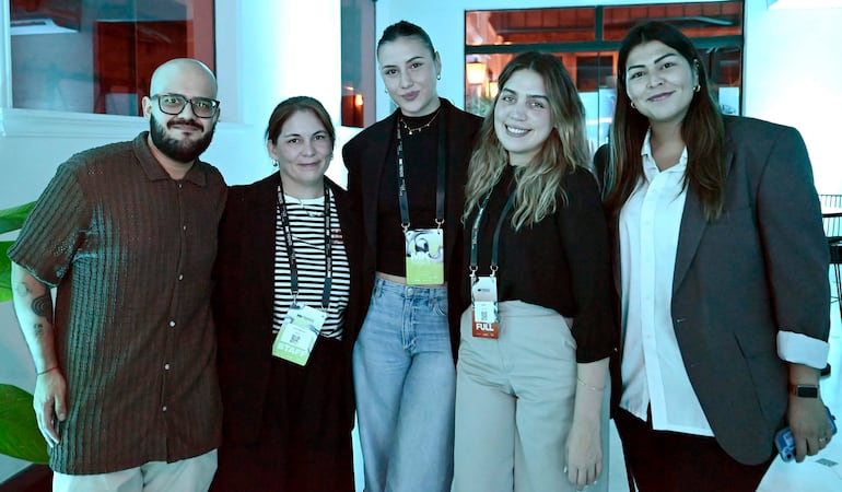 Cinco personas sonrientes, bien vestidas con gafetes, en un ambiente luminoso y elegante.