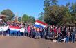 Grupo de personas, jóvenes y adultos, en manifestación con banderas paraguayas y pancartas, en un ambiente exterior rural.