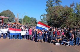 Grupo de personas, jóvenes y adultos, en manifestación con banderas paraguayas y pancartas, en un ambiente exterior rural.