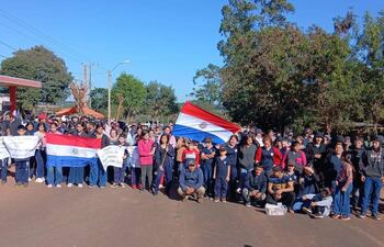 Grupo de personas, jóvenes y adultos, en manifestación con banderas paraguayas y pancartas, en un ambiente exterior rural.
