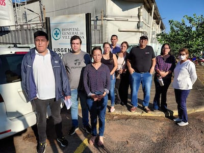 Grupo de diez personas, incluidas una mujer con bata blanca y hombres en chaquetas, reunidos frente al Hospital General de Villarrica.
