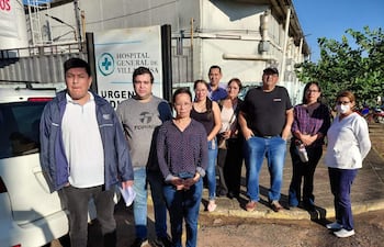 Grupo de diez personas, incluidas una mujer con bata blanca y hombres en chaquetas, reunidos frente al Hospital General de Villarrica.