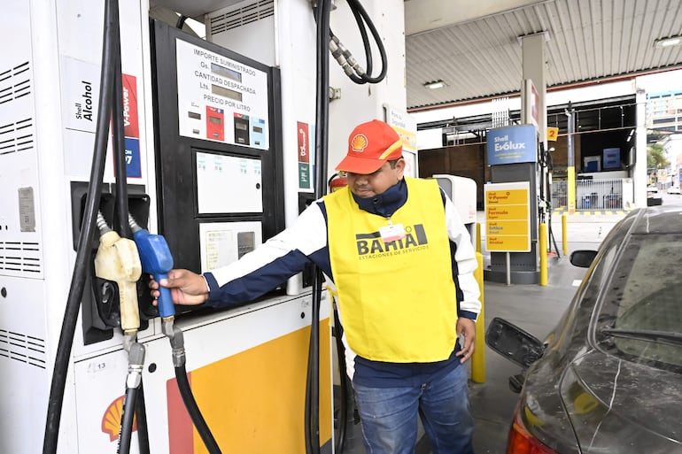 Hombre con chaleco amarillo de BAMTA y gorra roja Shell, despachando combustible en estación al aire libre.