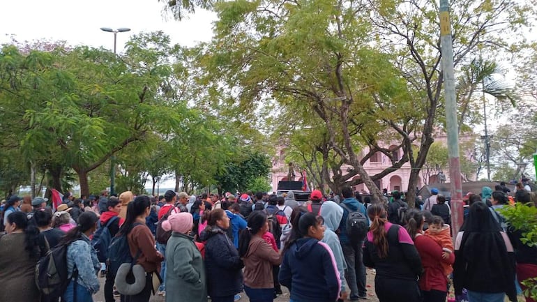 Multitud de personas reunidas en un espacio verde, algunas sosteniendo banderas, en un ambiente de protesta.