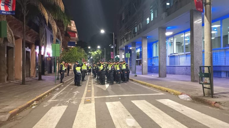 Grupo de policías en formación con uniformes oscuros y chalecos reflectantes, en una calle urbanizada iluminada.