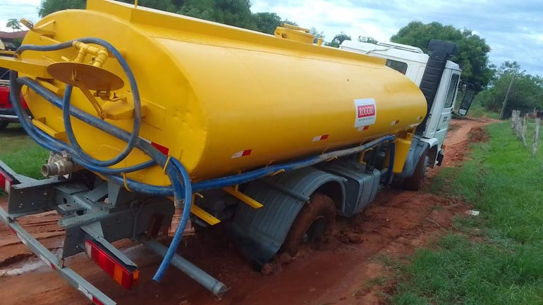 Camión cisterna amarillo atascado en camino de tierra, con tuberías azules y logotipo 'ROGGIO'. Entorno con vegetación y barro.