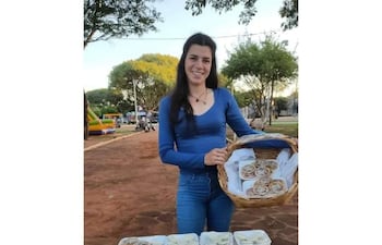 Diana Cañete, mujer de pie con camisa azul y jeans, sostiene canasta de pasteles frente a bandejas llenas en un parque.