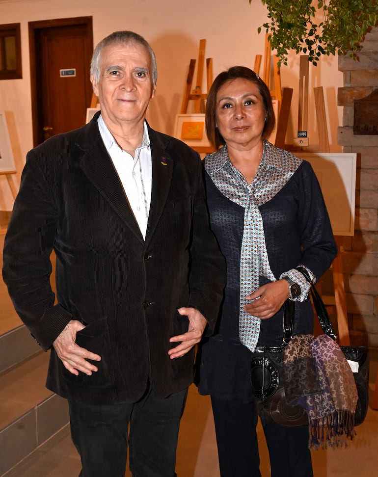 Juan Manuel Nungaray con cabello canoso y chaqueta oscura junto a mujer de atuendo azul marino en evento de arte.