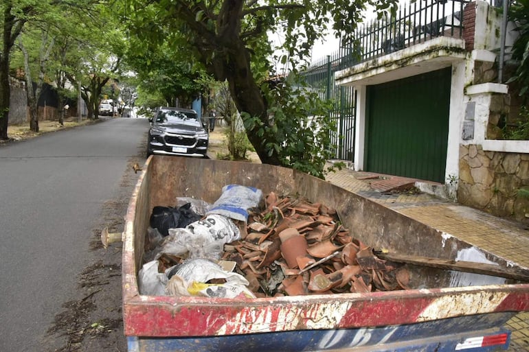 Contenedor de basura en calle residencial de Ciudad Nueva, con restos de tejas, sin personas visibles.