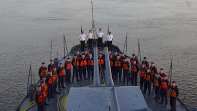 Grupo de personas uniformadas, algunos con chalecos salvavidas, sobre la cubierta de un buque militar en un ambiente acuático tranquilo.