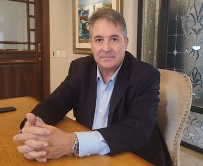 Édgar Melgarejo sentado en una mesa, con saco oscuro y camisa clara, manos entrelazadas en actitud tranquila.