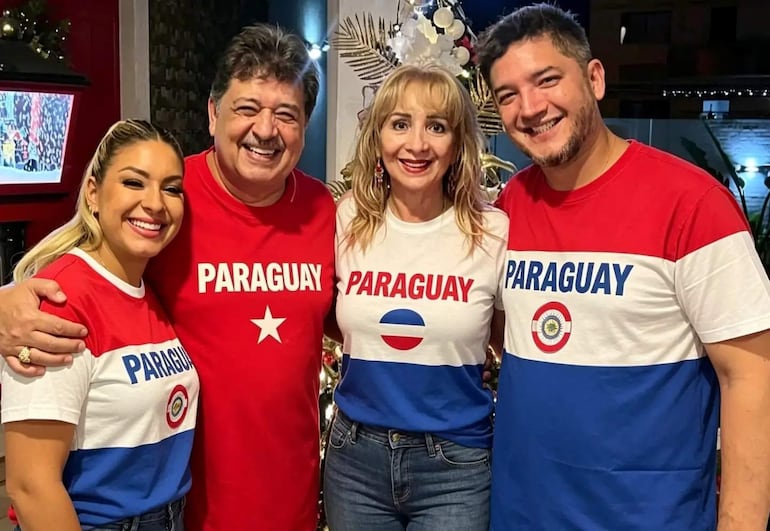 Cuatro personas sonrientes, dos hombres y dos mujeres, visten camisetas con la palabra 'PARAGUAY', en un ambiente interior festivo.
