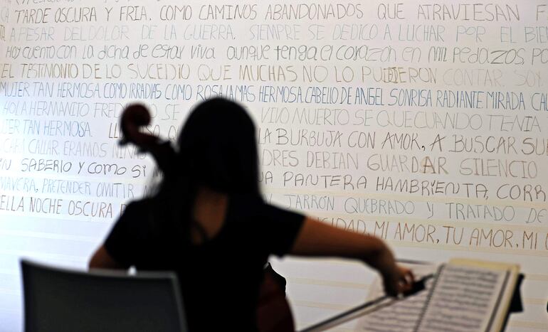Una persona mientras toca un violín frente a un poema en el muro de Fragmentos en Bogotá.