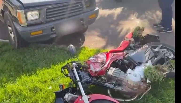 Motocicleta roja volcada sobre césped junto a camioneta oscura en el Puente de la Amistad. Sin personas visibles.
