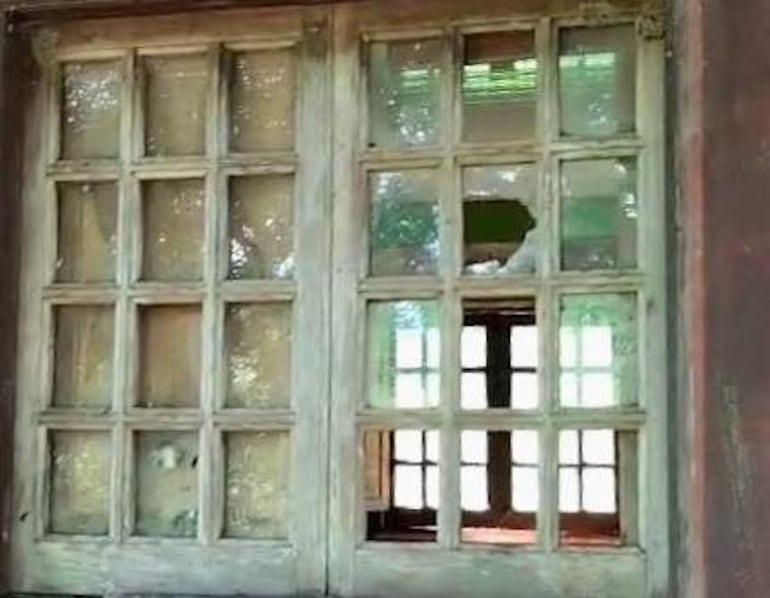 Ventana antigua con marco de madera roto y desgastado, con un área verde visible a través de ella.