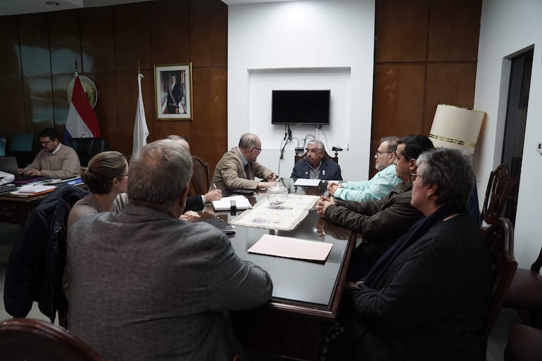 Isaías Fretes de cabello canoso y saco oscuro, discute en una mesa con participantes atentos en reunión formal.