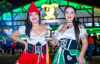 Dos mujeres sonrientes en trajes típicos, una sostiene una jarra de cerveza, con fondo iluminado.