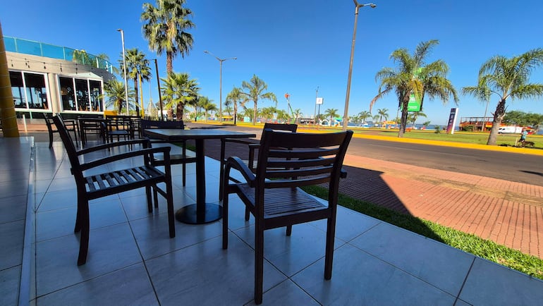 Ambiente exterior tranquilo con sillas de madera, palmeras y un sendero iluminado por el sol, sin personas presentes.