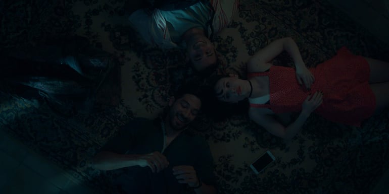 Diro Romero y Matías Miranda sonríen mientras escuchan a Lia Love, quien luce pensativa en vestido rojo.