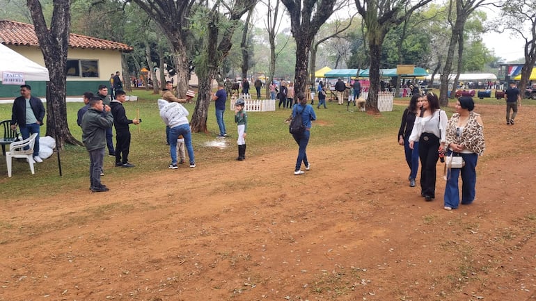 Niño con uniforme de jinete juega mientras cuatro adultos caminan, rodeados de carpas y naturaleza en evento de confraternidad.