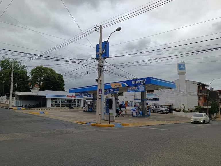 Estación de servicio Energy con techo azul y blanco, vehículos en movimiento bajo un cielo nublado.