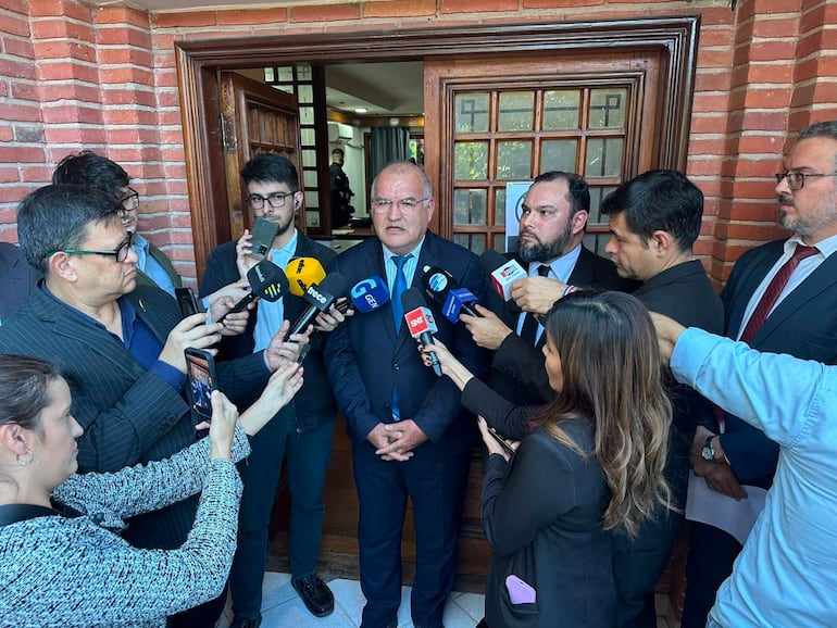 Walter Santiago Laguardia en chaleco y corbata respondía preguntas de varios reporteros en un ambiente exterior.