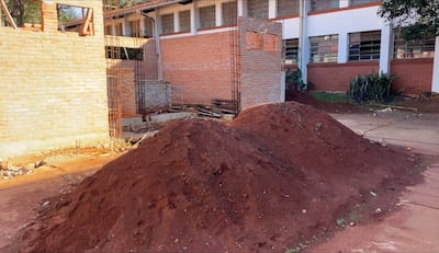 Montículos de tierra roja en obra sin finalizar en el CTN de Encarnación, con paredes de ladrillo al fondo y varillas expuestas.
