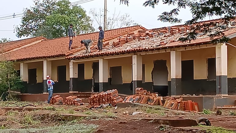 Cuatro hombres en el techo: dos de pie y uno agachado colocando tejas, mientras un cuarto supervisa desde el suelo.