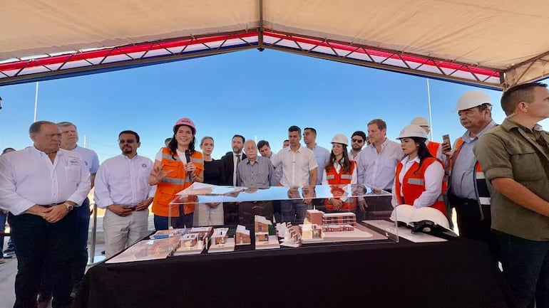 Claudia Centurión, con casco y chaleco naranja, presenta una maqueta frente a un grupo de personas en un evento al aire libre.