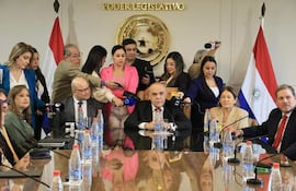 Grupo de personas sentadas alrededor de mesa, discutiendo el presupuesto. Banderas de Paraguay y el emblema del Poder Legislativo en el fondo.