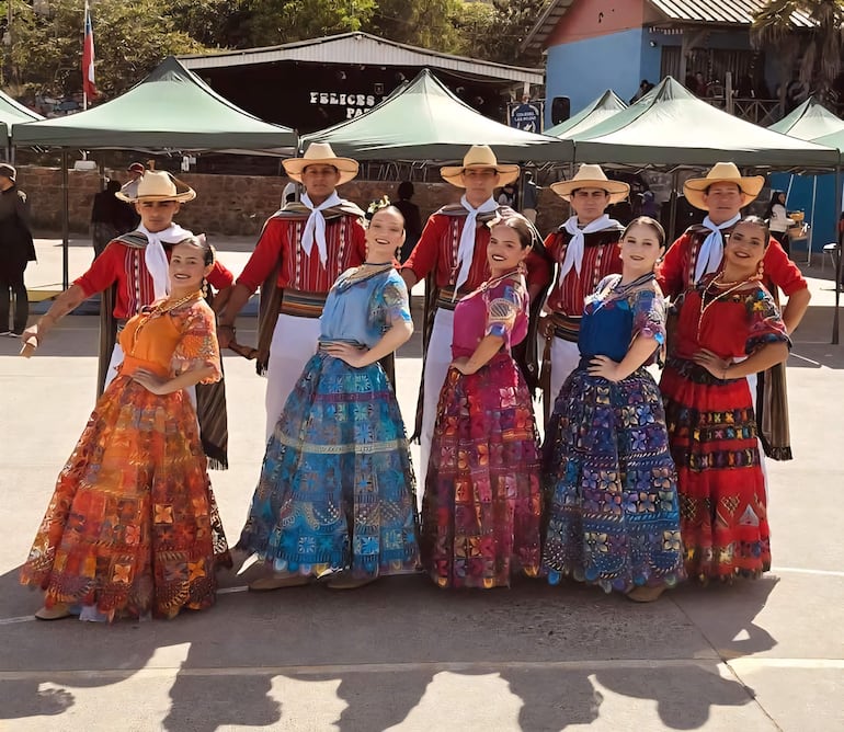Grupo de ocho personas en trajes tradicionales: mujeres en vestidos coloridos y hombres con camisas rojas y sombreros, sonriendo festivamente.