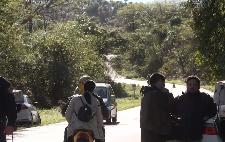 Varias personas en la carretera, un hombre con casco dorado conversa con otros, rodeados de vegetación.
