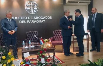 El doctor Manuel Riera Escudero recibe la distinción de manos de su hijo Manuel Riera. El ministro del Interior, Enrique Riera (izq.) y el presidente del Colegio de Abogados, Jorge Arturo Daniel, observan la escena.