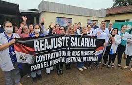 Grupo de médicos en uniforme sosteniendo pancarta que dice 'REAJUSTE SALARIAL' durante la protesta frente al hospital.