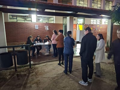 Seis personas en cafetería, cuatro mujeres sentadas trabajando y hombres de pie conversando en un ambiente colorido y relajado.