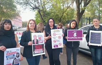 Seis mujeres, algunas con carteles, protestan con expresiones decididas en un espacio urbano.