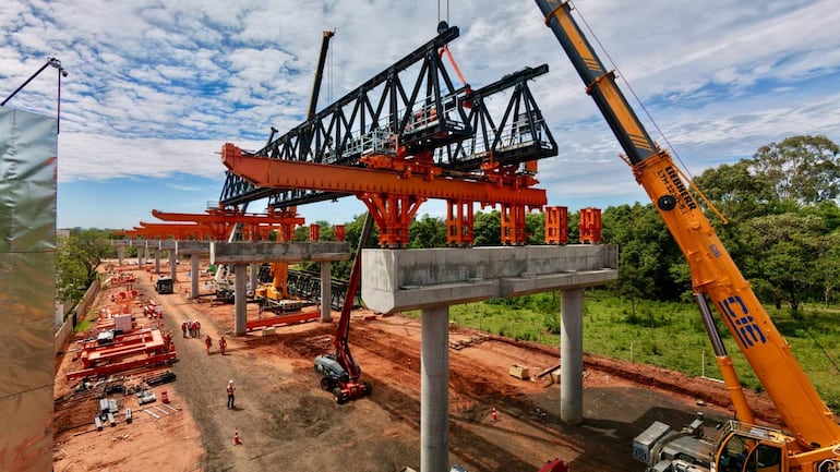 Trabajadores en cascos y ropa de obra operan grúas y manipulan soportes de viga metálica en un entorno de construcción.